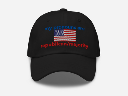 A black dad hat with the embroidered text "my pronouns are republican/majority" in bold red and blue, featuring a detailed American flag design at the center, viewed from the front