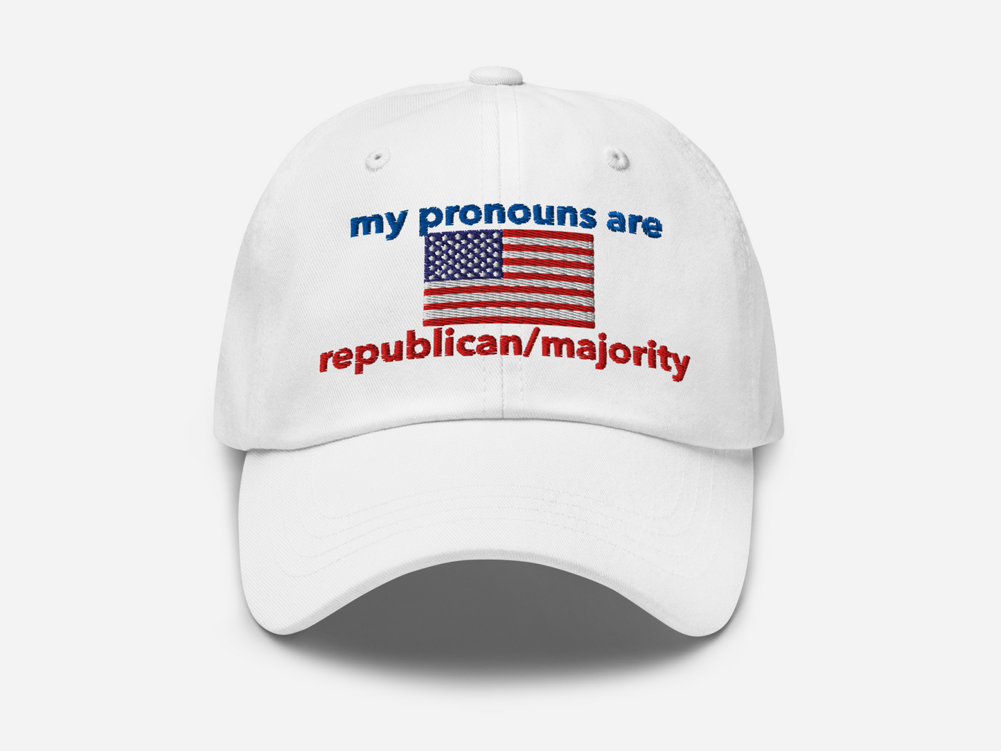 A white dad hat with the embroidered text "my pronouns are republican/majority" in bold red and blue, featuring a detailed American flag design at the center, viewed from the front